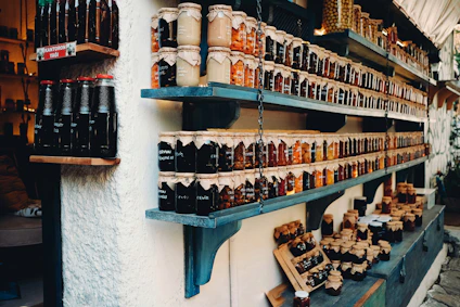 Colorful jars of homemade preserves and pickles lined up neatly on a blue-painted wall shelf.