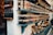 Shelves filled with a variety of jars containing preserves and sauces, labeled and neatly arranged. The jars are topped with brown paper and tied with string. There are different colors and types of preserves, creating a rustic and artisanal market display.