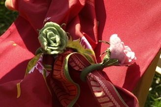 A red fabric with floral patterns is draped over a surface. Two fabric flower napkin rings, one green and one pink, are secured around the fabric, adding decorative elements.