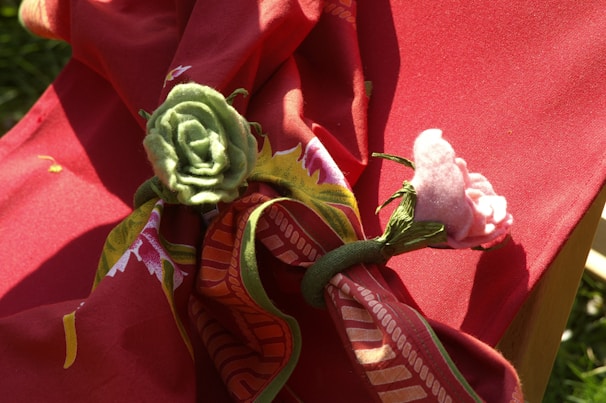 A red fabric with floral patterns is draped over a surface. Two fabric flower napkin rings, one green and one pink, are secured around the fabric, adding decorative elements.