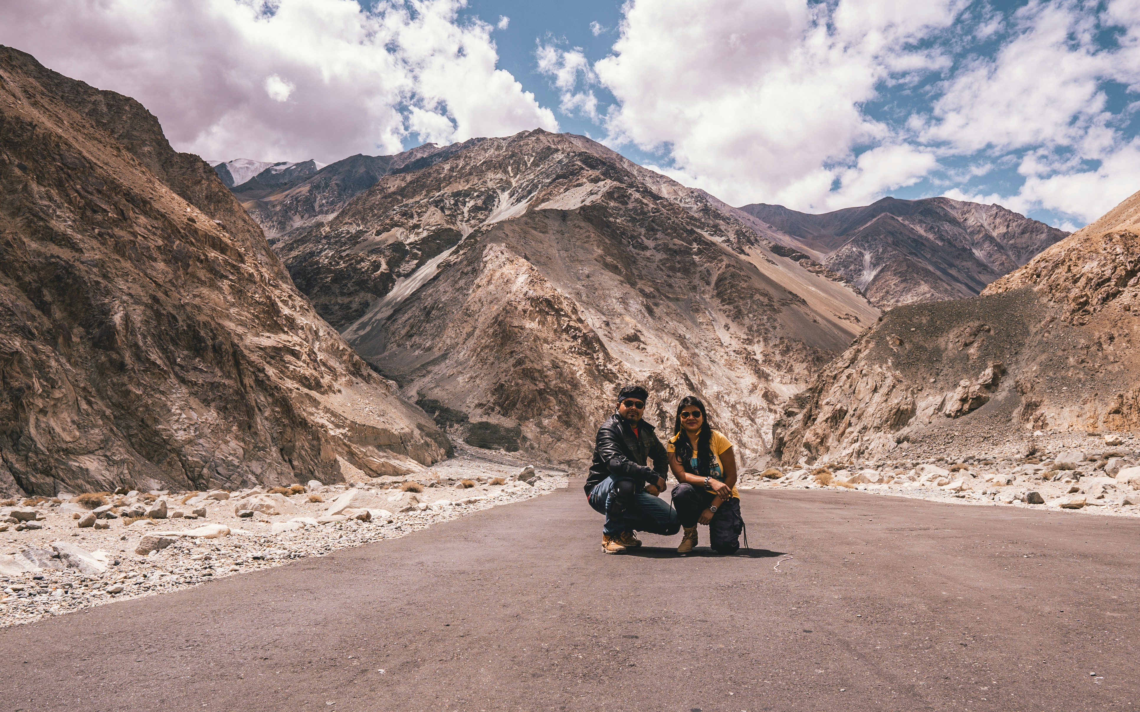 two man and woman crouching in middle of road during daytime
