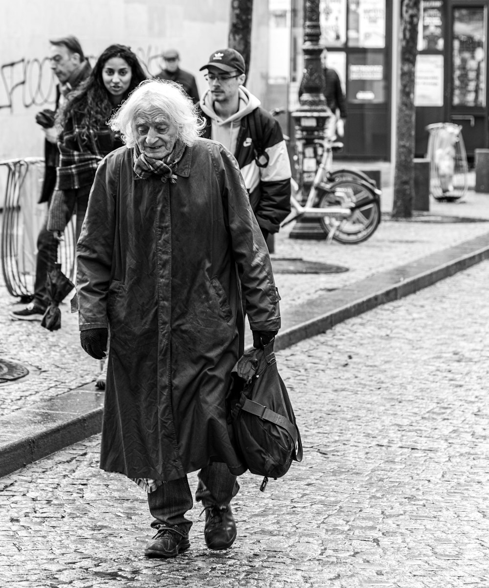 grayscale photography of man wearing coat carrying bag