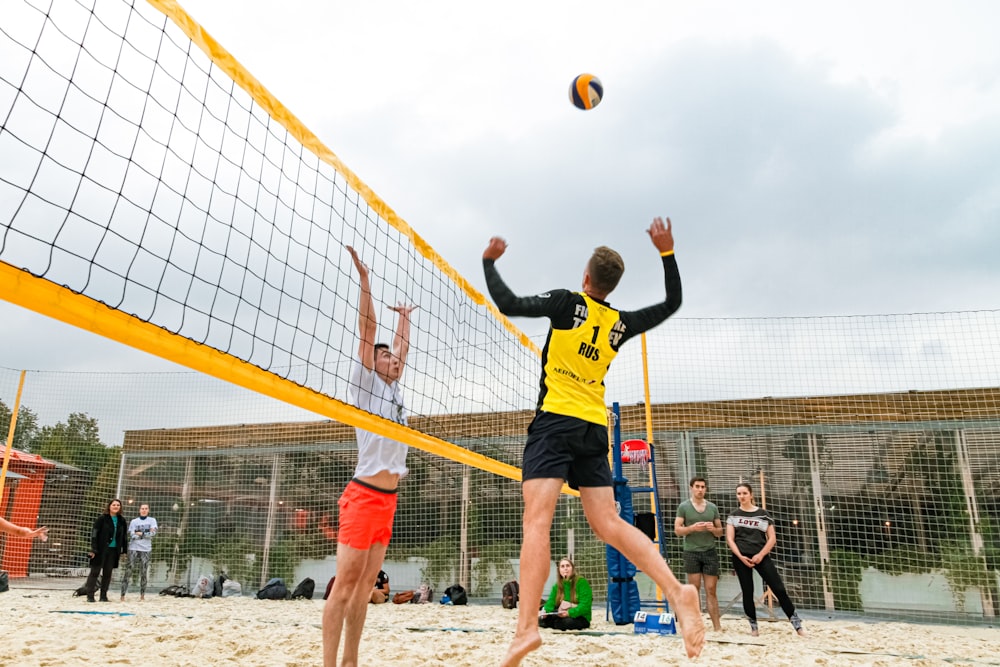 uomo che indossa una maglietta a maniche lunghe gialla e nera che gioca a pallavolo