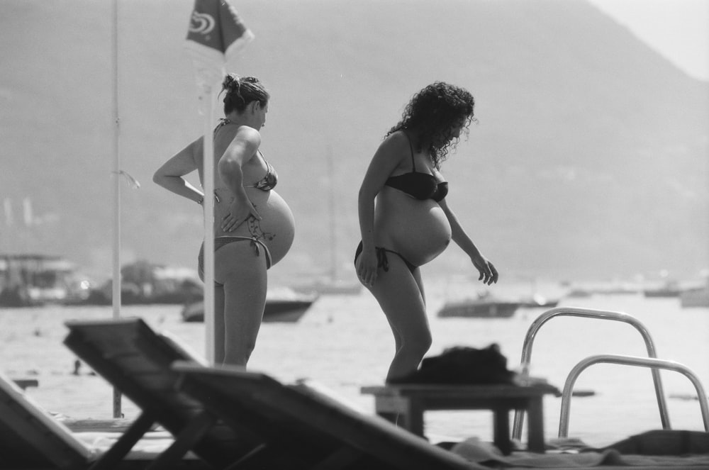 grayscale photography of two pregnant women enjoying on beach