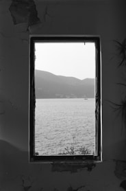 grayscale photo of body of water through glass window