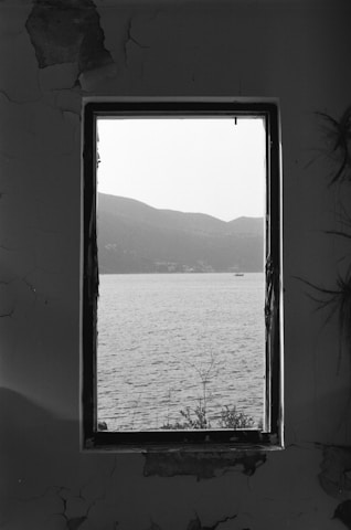 grayscale photo of body of water through glass window