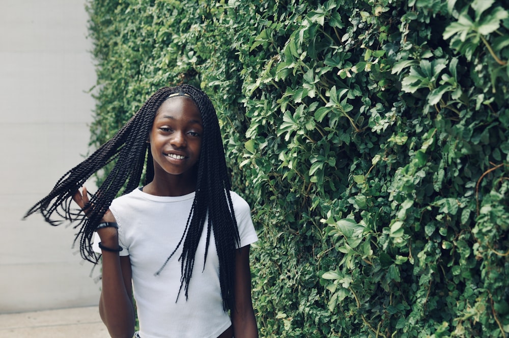 standing and smiling woman wearing white shirt beside green plants