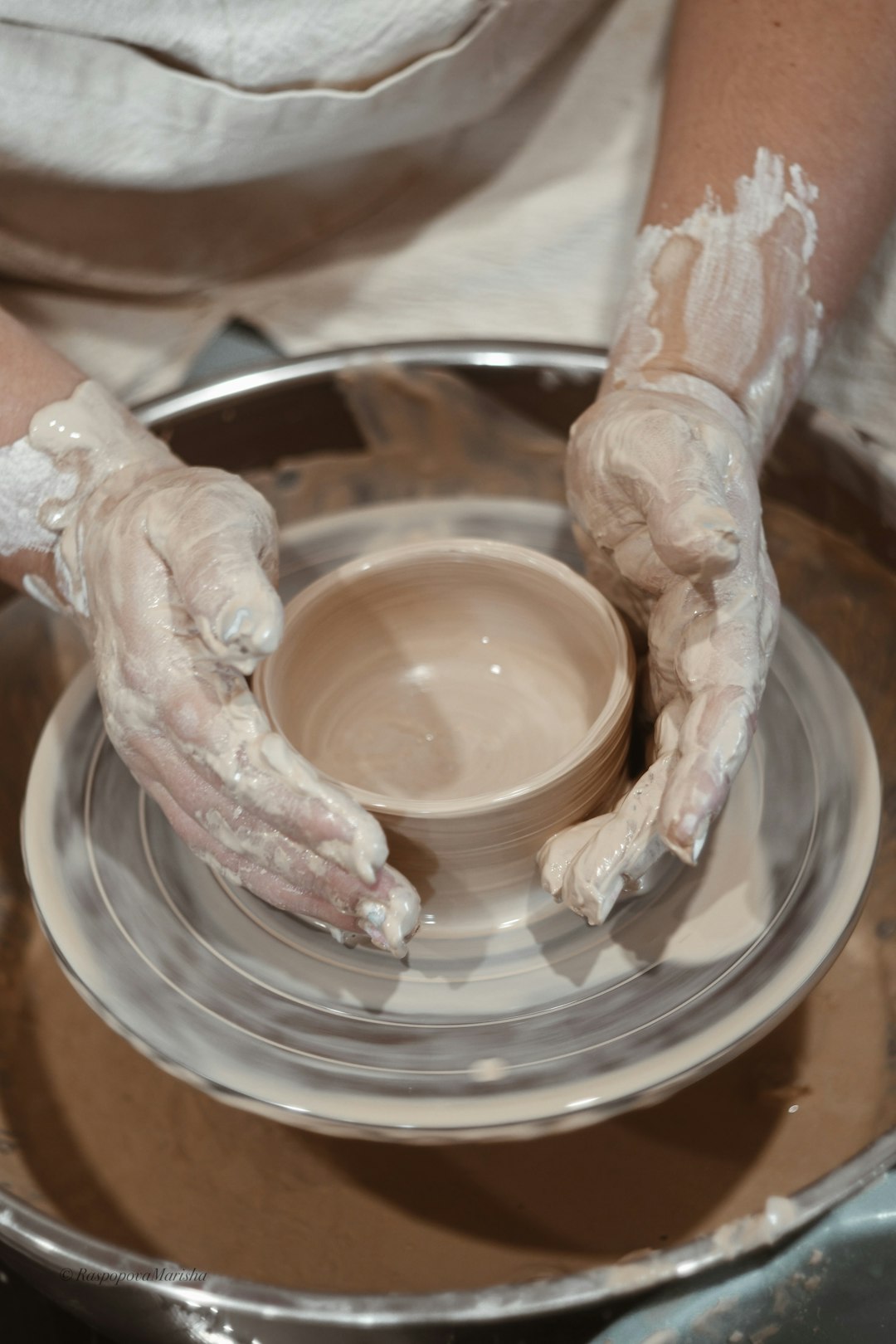 person forming a bowl out of fresh clay on spinning machine
