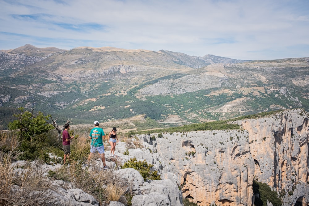 three people standing on cliff during daytime