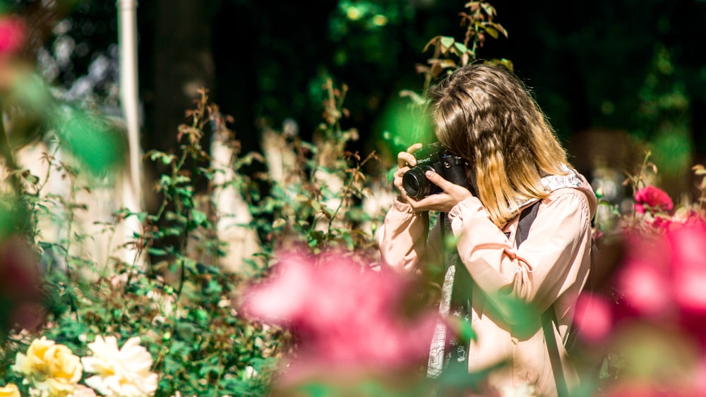 fotografía de enfoque selectivo de mujer sosteniendo una cámara DSLR negra durante el día