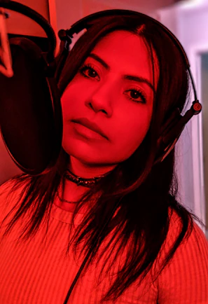 Lhiannon Leigh in a cozy recording studio, eyes glowing softly behind vintage-style headphones.