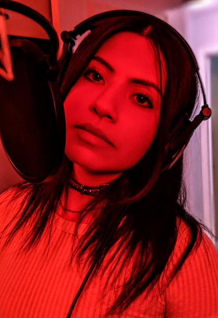 Behind-the-scenes shot of Carolina Redd recording voice overs in a cozy home studio filled with warm lighting and soundproofing panels.
