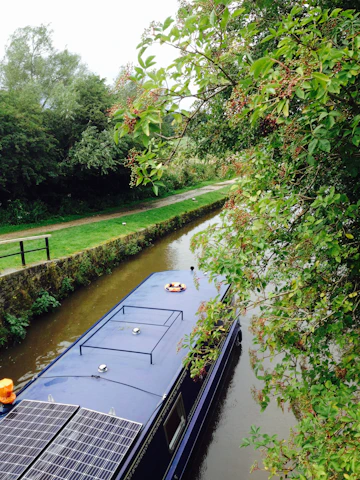 A sleek turquoise electric canal boat cruising gently along a classic narrow canal lined with lush greenery.