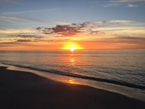 Sunset over the serene beach with vibrant orange hues reflecting on calm waters