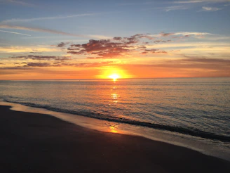 Sunset over the serene beach with vibrant orange hues reflecting on calm waters