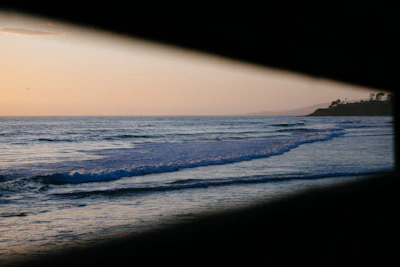 A quiet beach at dusk, waves gently lapping the shore under a sky painted with soft pastel hues.