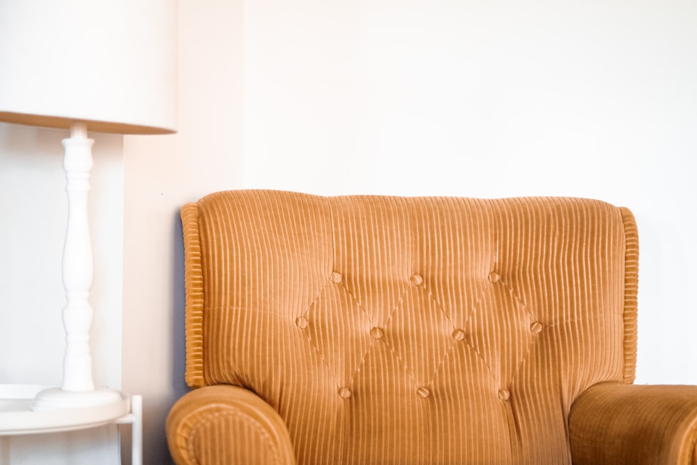 tufted brown fabric sofa chair beside white table lamp on white end table