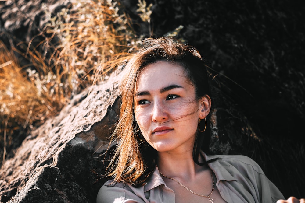 woman wearing brown collared top leaning on brown stone