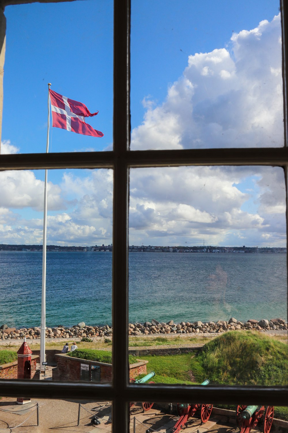 日中、海の近くの大砲や木々の上のポールの上にデンマークの国旗