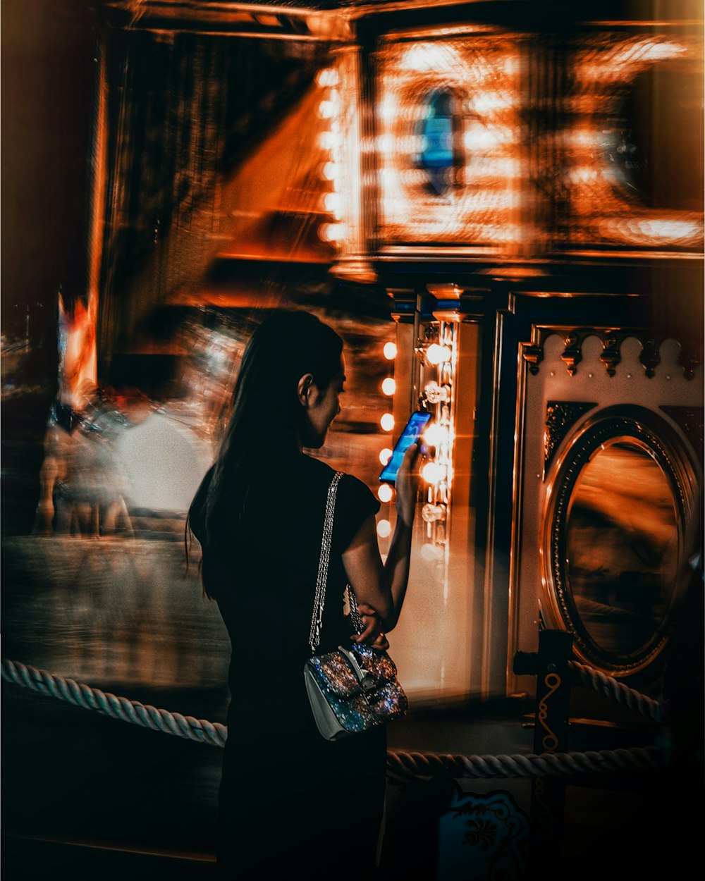 Zeitrafferfotografie einer Frau, die ein Smartphone vor einem Karussell hält