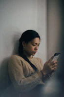woman leaning back on white wall and using smartphone