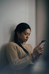 woman leaning back on white wall and using smartphone
