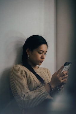 woman leaning back on white wall and using smartphone