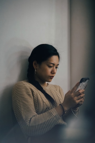 woman leaning back on white wall and using smartphone