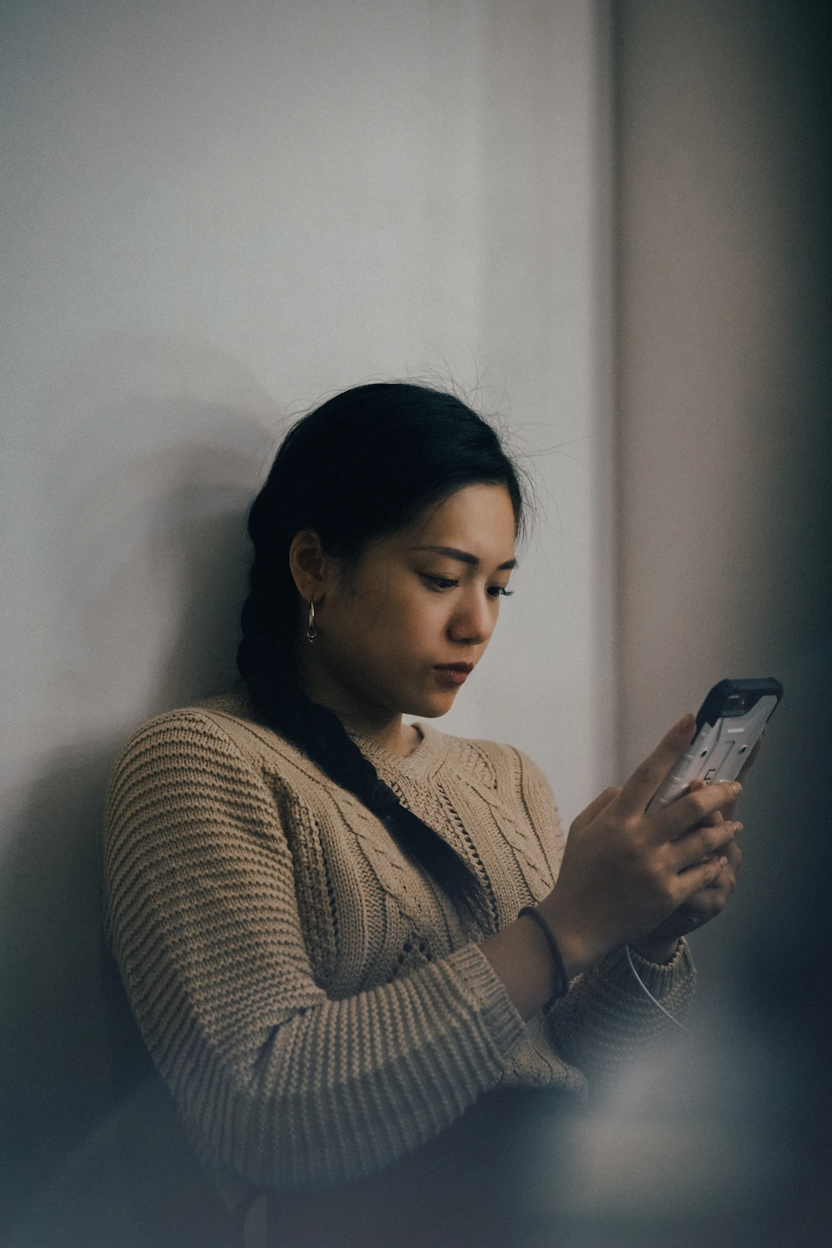 A woman in a cream knitted jumper reading something on her phone, thoughtful, soft indoor light