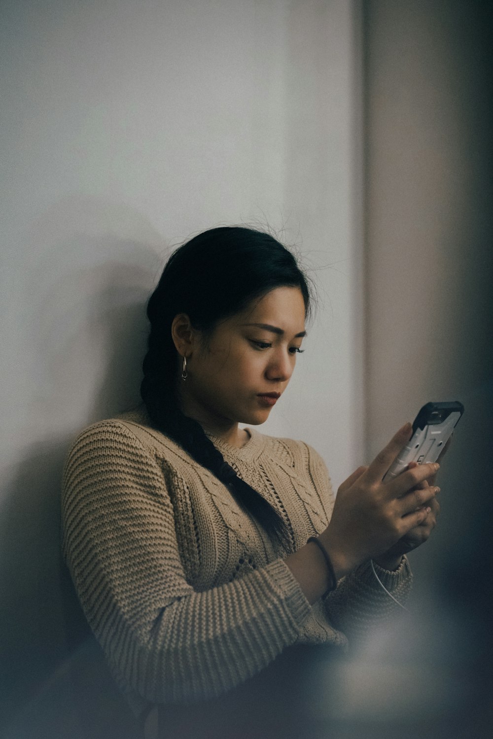 woman leaning back on white wall and using smartphone