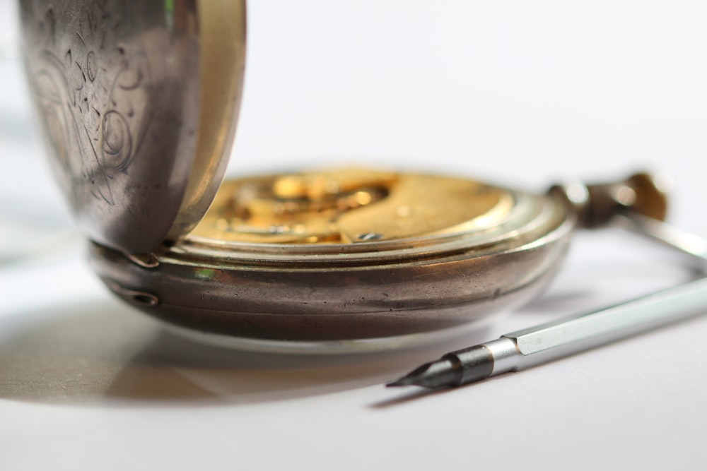 round gold-colored pocket watch beside pen
