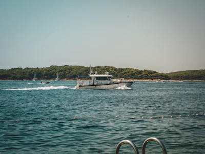 A marine security patrol boat cruising actively along the coastline under a clear blue sky.