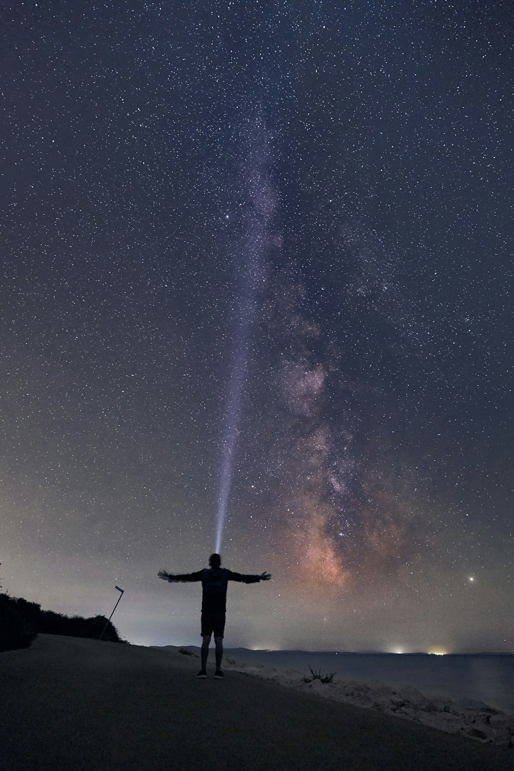 a man standing on top of a sandy beach under a night sky filled with stars