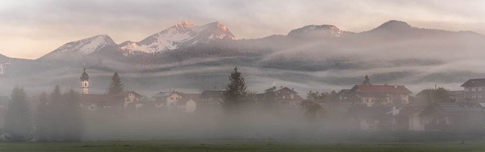 un paysage brumeux avec des maisons et des montagnes en arrière-plan