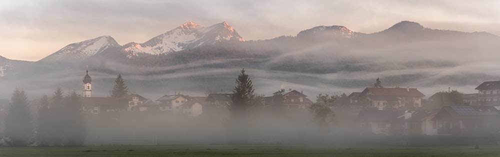a foggy landscape with houses and mountains in the background