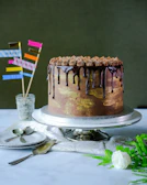 Close-up of a chocolate drip cake with gold leaf accents and a soft pink background.