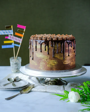 Close-up of a chocolate drip cake with gold leaf accents and a soft pink background.