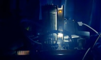 A close-up view of computer hardware in a dimly lit environment, featuring components like a cooling fan and wires. The scene is bathed in blue light, creating a futuristic and tech-focused atmosphere.