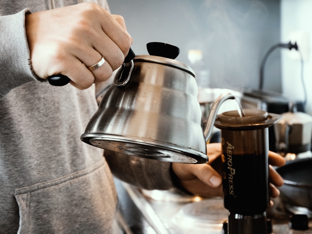 person holding stainless steel teapot