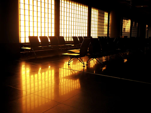A sleek airport lounge seating area with black leather chairs and gold accents bathed in soft natural light.