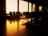 An empty airport waiting area with rows of chairs is bathed in warm, golden light from large backlit glass windows. The polished floor reflects the glow, creating a tranquil atmosphere.