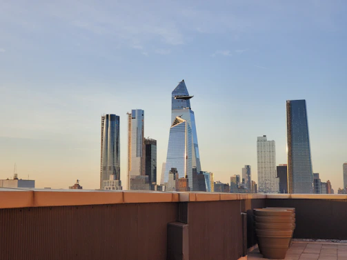 A futuristic city skyline at dawn, with green rooftop gardens and clear blue skies.