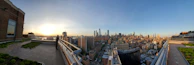 A panoramic view of a city skyline at sunset, seen from a high-rise balcony.