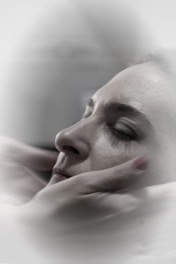 A close-up of a person with closed eyes, being gently cradled by hands which suggest a comforting or soothing gesture. The soft focus and muted colors create a calm, serene atmosphere.