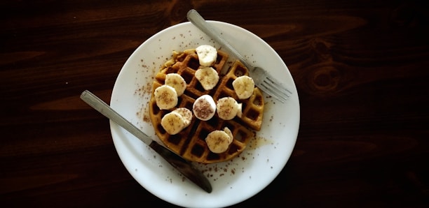 waffle with sliced banana fruits on top near gray stainless steel fork and knife
