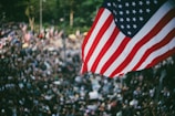 A crowd waving American flags at a Trump rally, red-white-blue banners visible.