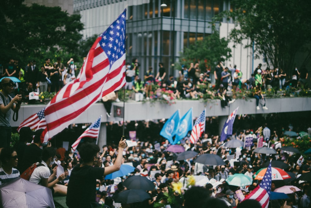 Uma multidão de pessoas segurando bandeiras e guarda-chuvas americanos
