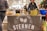 A market stall with a banner featuring the text 'Restaurant Bar Sternen' displayed. Various beverages are organized in ice buckets including a blue Ciroc bucket, and there are snacks on the table, possibly samples. People are standing around the stall in casual clothing.