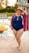 A person wearing a blue one-piece swimsuit and a wide-brimmed hat, standing by the edge of a swimming pool. They have a colorful, patterned cover-up draped over their shoulders and appear to be smiling joyfully. In the background, several inflatable rings float in the pool, and a waterslide is visible, suggesting a lively and fun summer setting.