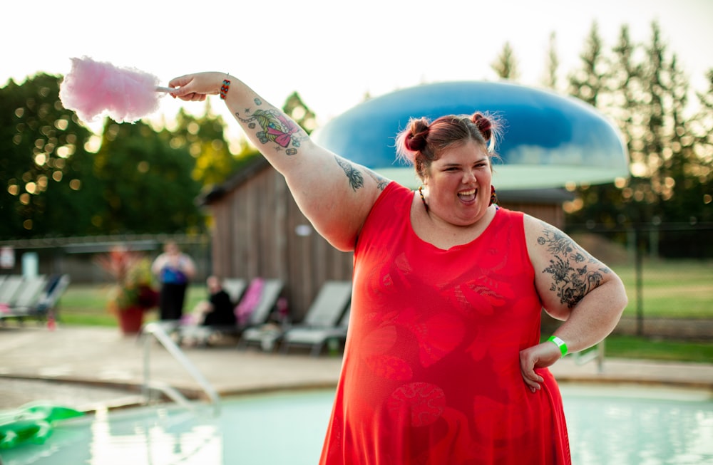 Fat woman in red dress near pool smiling and holding candy floss